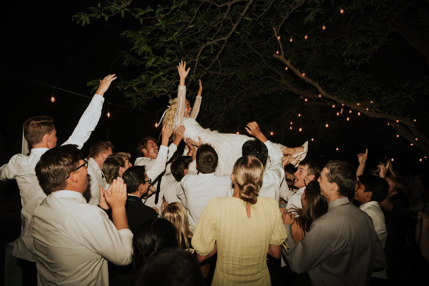 Bride lifted by guests under string lights
